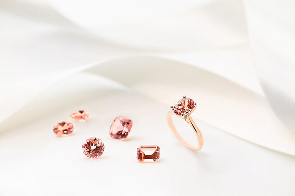 lab created champagne pink sapphires in various shapes and sizes next to a rose gold solitaire engagement ring with 1ct oval cut pink sapphire